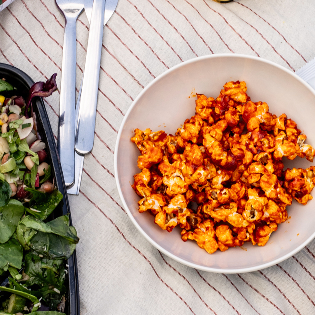 Close-up of gochujang popcorn in a bowl, showing golden, fluffy popcorn coated in a vibrant, reddish-orange glaze. The popcorn looks crisp with a slight sheen, hinting at a spicy-sweet flavor from the gochujang sauce.