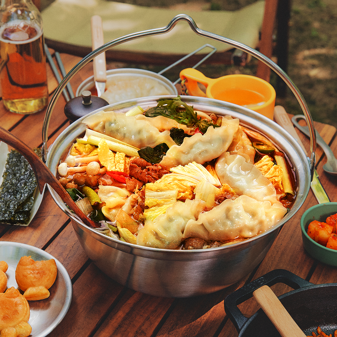 A close-up of a hotpot filled with savory broth, mandu dumplings, fresh vegetables, and colorful ingredients.