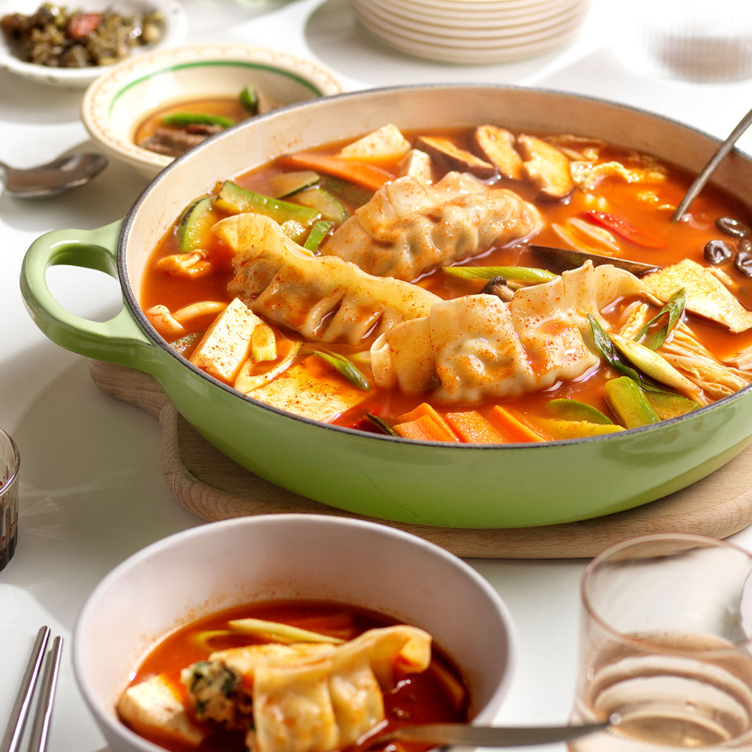 A flavorful pot of kimchi dumpling stew with tofu and vegetables, showcasing a rich broth filled with dumplings, vibrant vegetables, and tender tofu, all simmering together in a comforting, aromatic dish.